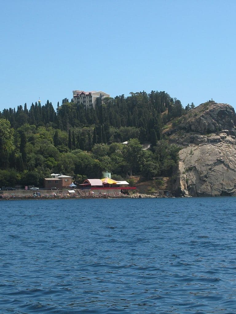 Мыс Плака с моря: скальный купол, кипарисы на склоне и башня дворца над берегом