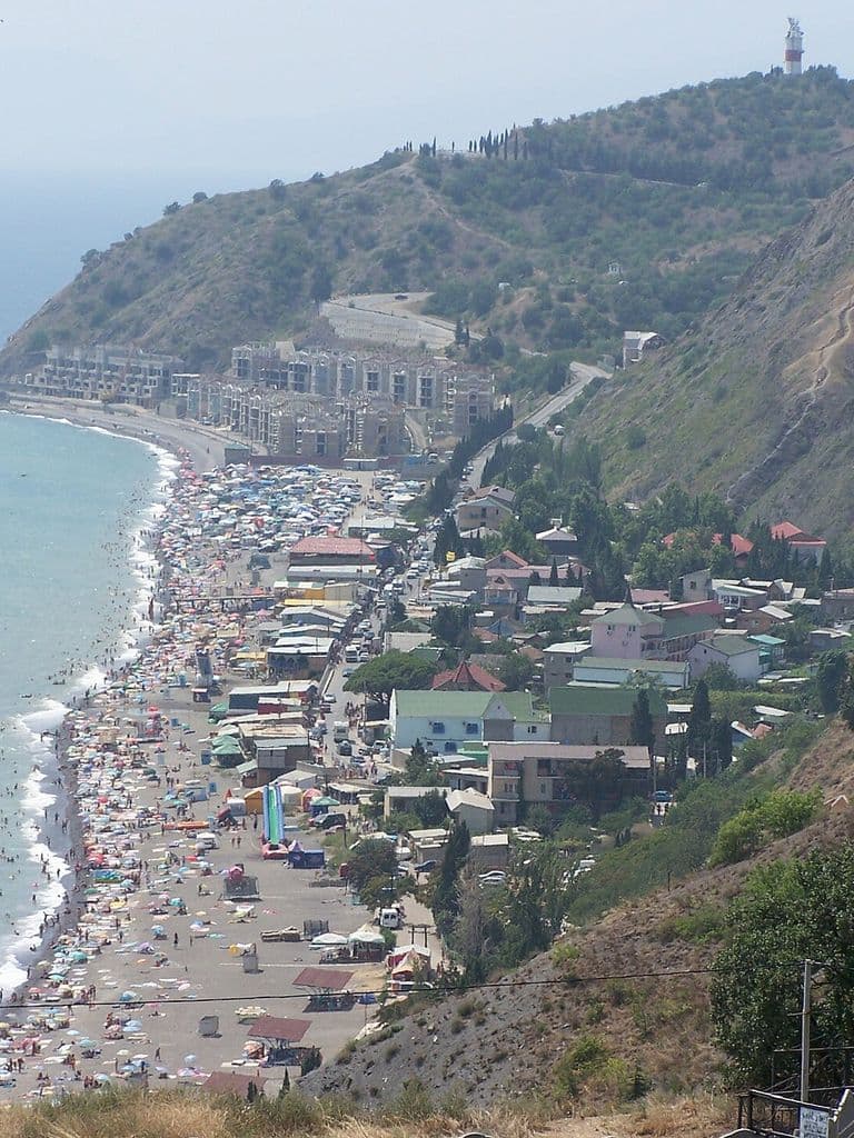 Вид сверху на село Рыбачье, длинный пляж вдоль моря и холмистый мыс