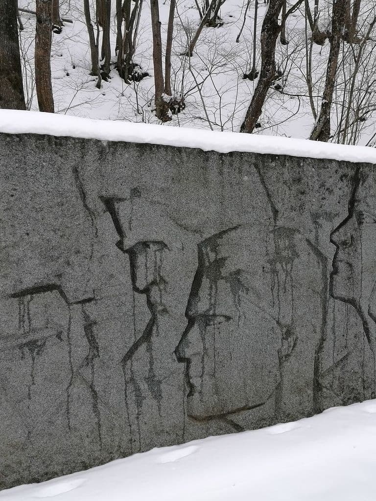 Гранитная стела мемориала «Партизанская шапка» с рельефными профилями партизан