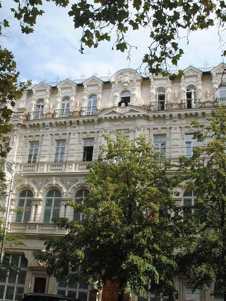 Нарядный светлый фасад бывшего доходного дома Гавалова на проспекте Нахимова, 9 в Севастополе, где размещён художественный музей, за кронами деревьев
