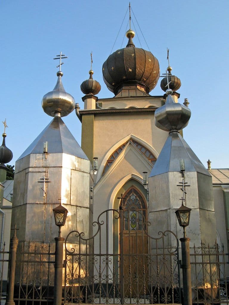 Храм Феодора Стратилата в Алуште: стрельчатый готический портал за кованой оградой и серебристые луковичные купола со звёздами в вечернем свете