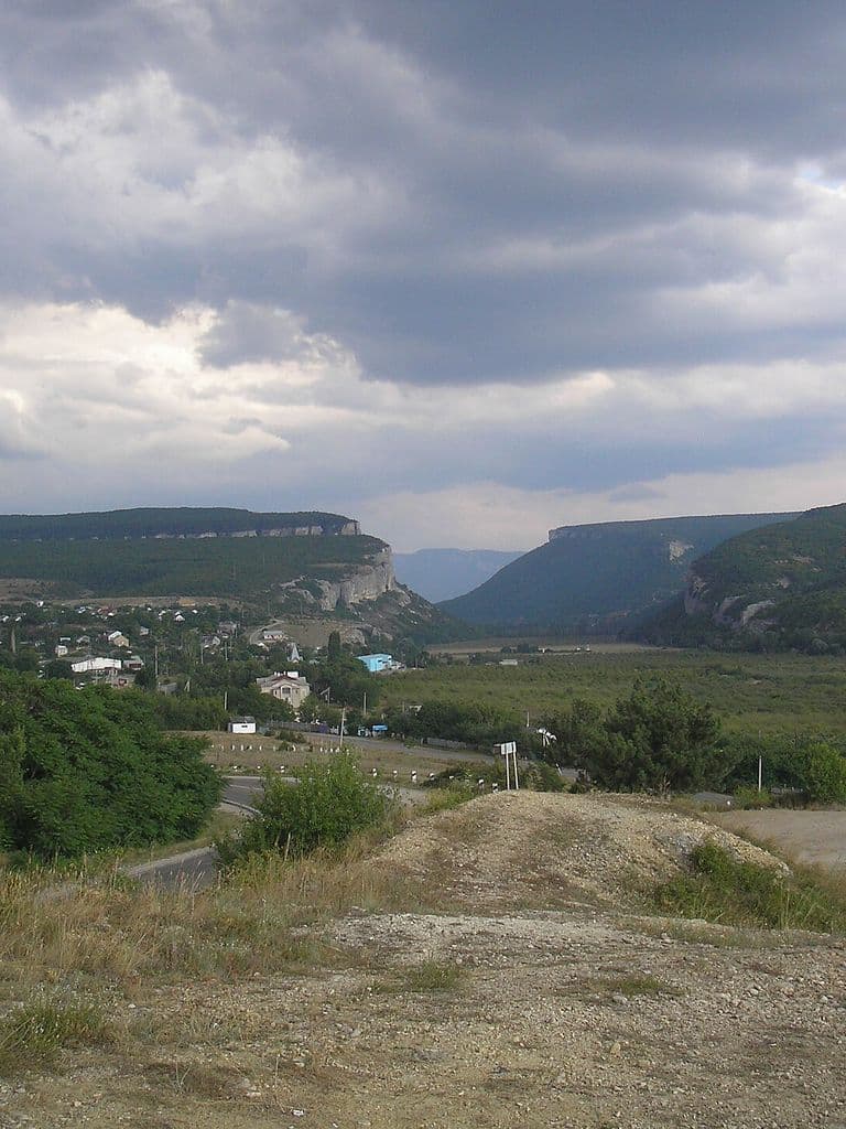 Село Танковое в Бельбекской долине: дома среди зелени у подножия белых известняковых обрывов под облачным небом