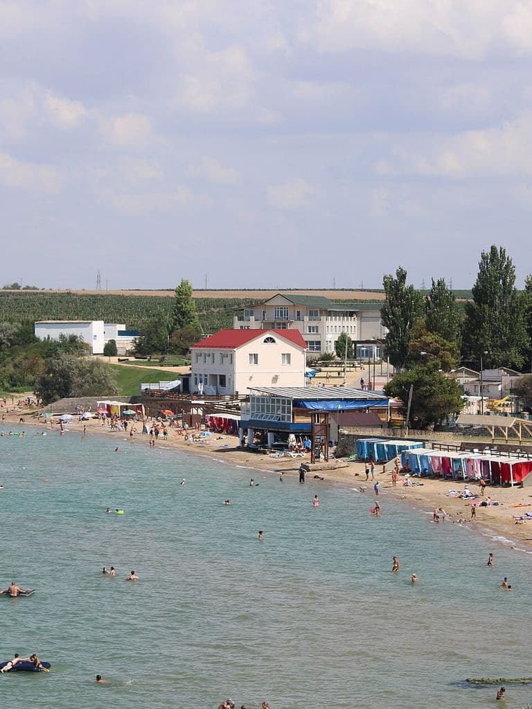 Пляж в Угловом на Каламитском заливе: купальщики у берега, пляжные навесы, дома и тополя над обрывистым берегом