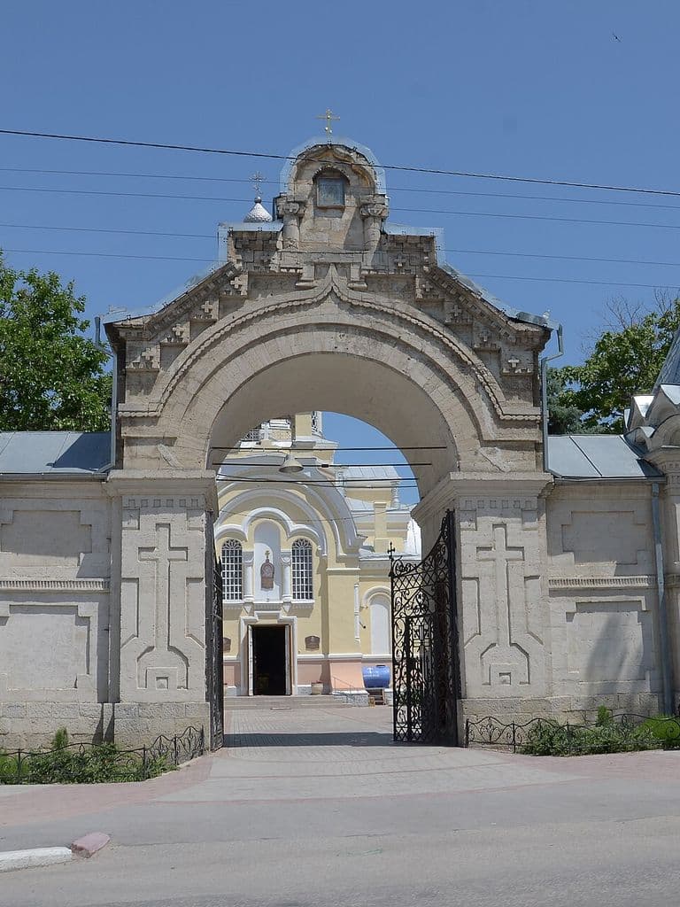Белые резные ворота с шатровыми башенками и иконами на территорию Казанского собора в Феодосии; в арке виден сам собор